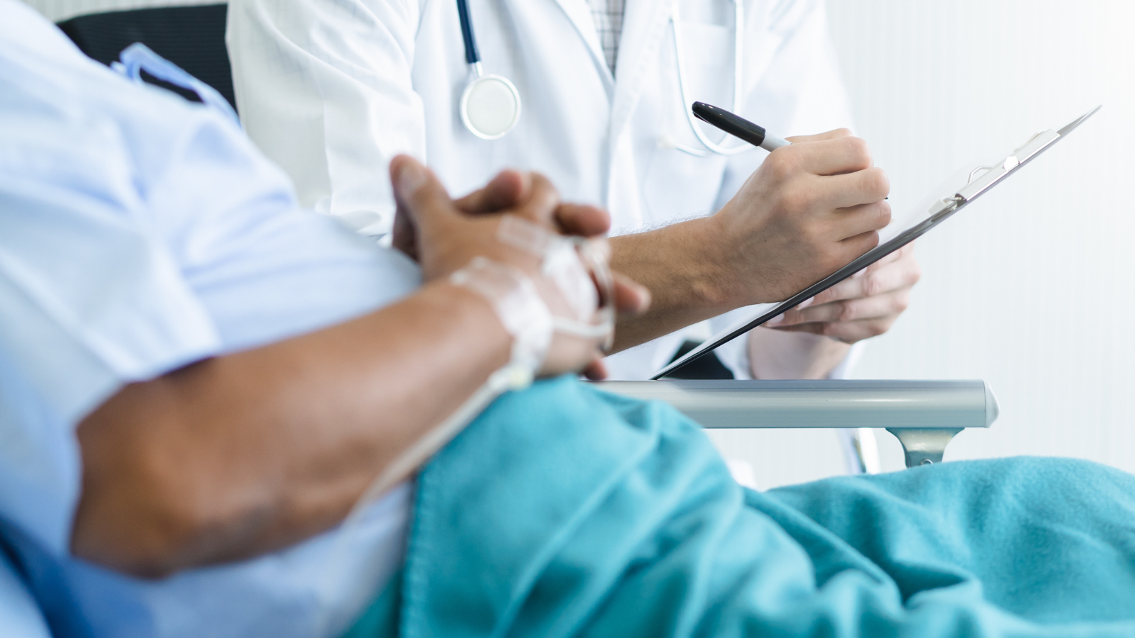 A patient sits in bed next to a doctor with a clipboard.