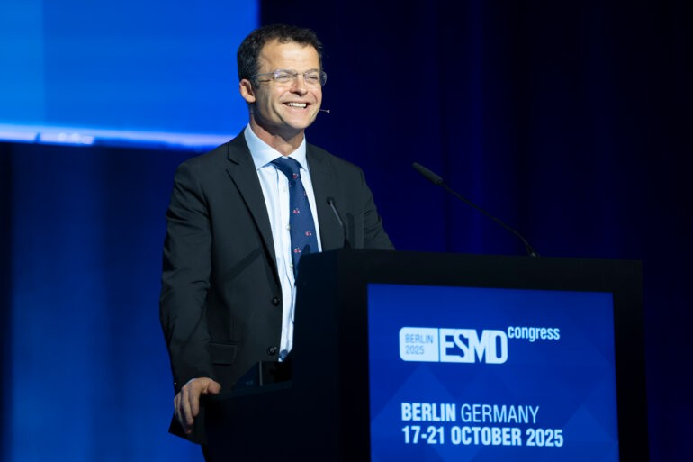 Professor Thomas Powles stands smiling in front of a lecturn, giving a presentation