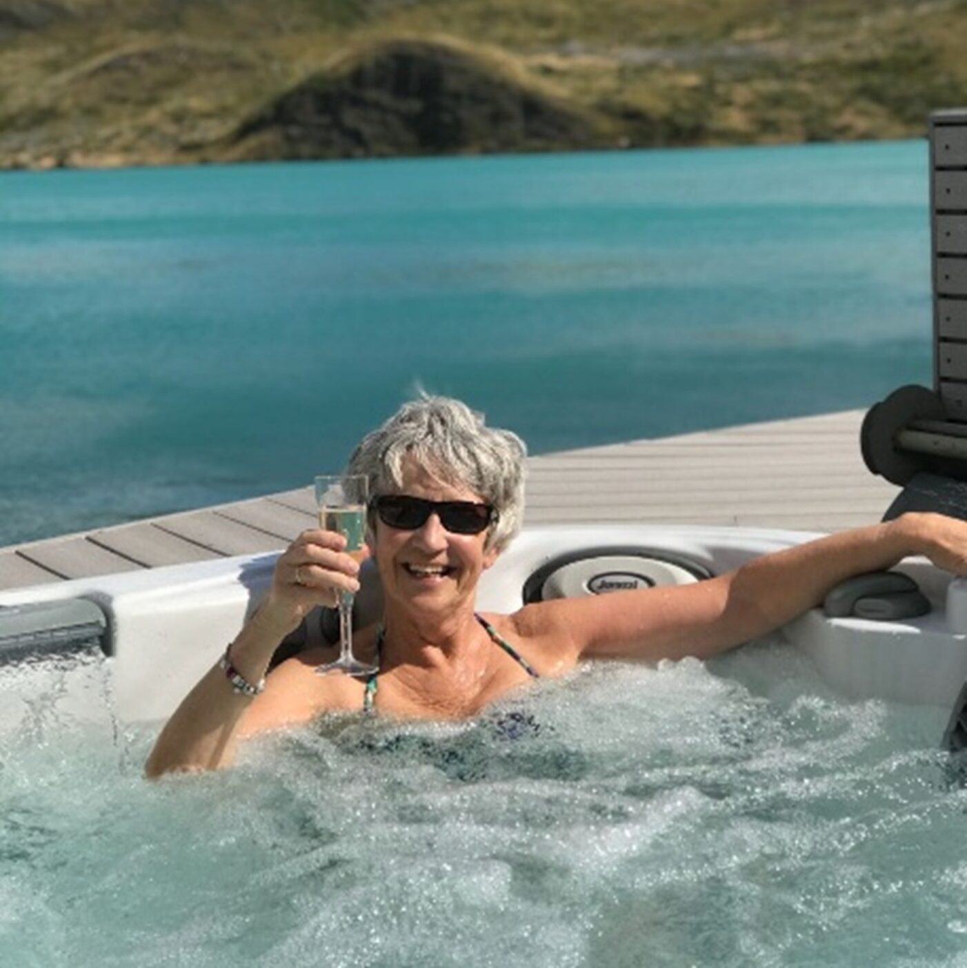 A woman sits submerged in a hot tub holding a champagne flute up to the camera